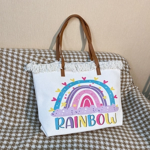 Detail of white canvas tote with rainbow print, fringe trim and brown handles