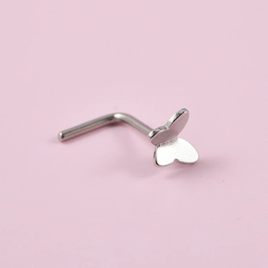Macro detail of a silver butterfly nose stud made of stainless steel on a pink background
