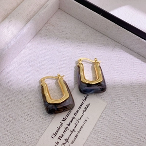 Detailed view of U-shaped gold-plated earrings with dark marble resin inlays on fabric