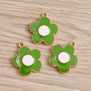 Three green and white enamel daisy flower pendants with gold plating on wood background