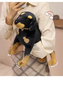 Close-up of soft black and tan realistic puppy plush toy held in hands for size reference
