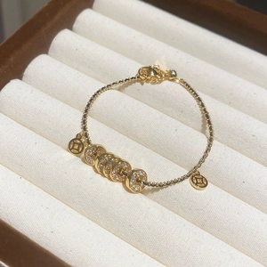 Gros plan d'un bracelet plaqué or 18k avec breloques pièces et cristaux en écrin