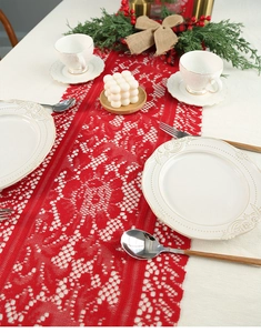 Detail of red festive lace table runner with intricate floral patterns and Christmas decor