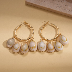 Detail of gold hoop earrings with hanging natural shell pendants on stone background