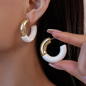 Close-up of stylish C-shaped acrylic earrings with gold metal studs shown on model