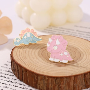 Cute blue stegosaurus and pink triceratops enamel pins on a natural wood base