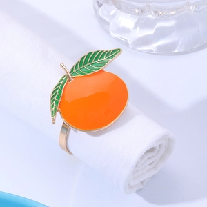 Close-up of a golden orange fruit napkin ring with enamel details on a white cloth