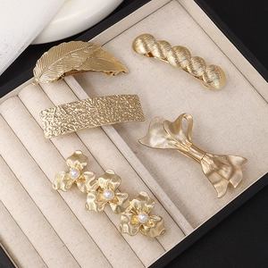 Detailed view of 5 golden metal hair clip styles with leaf and pearl designs