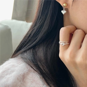 Detail shot of silver twisted knot ring and heart dangle earrings on model