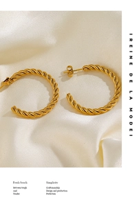 Détail des boucles d'oreilles créoles torsadées dorées sur fond de soie élégant