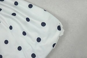 Close-up of soft white fabric with black polka dot print and pleated texture detail