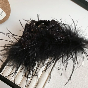 Detail of elegant black feather hair claw clip with sequins on a beige jewelry tray