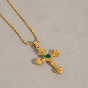 Détail d'une croix dorée vintage avec gemme cœur verte et motifs de roses gaufrés