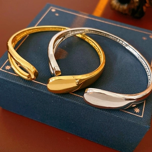 Close-up of gold and silver teardrop open bangles on a textured navy jewelry box