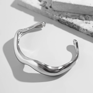 Close-up of a silver irregular wavy cuff bracelet with a polished finish and artful curves