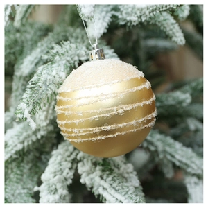 Macro detail of golden Christmas ball with white glitter stripes on snowy pine branch