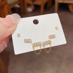 Close-up of three pairs of gold-plated zircon earrings with tassels on a display card