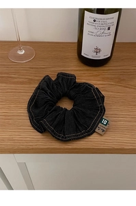 Detail of premium denim hair scrunchie with yellow stitching on a rustic wooden desk