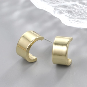 Close-up of golden C-shaped hoop earrings with a mirror-polished finish on glass