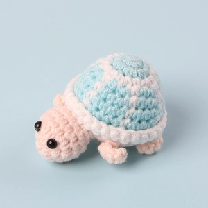 Detailed close-up of a handmade pink crochet turtle doll with a blue and white shell