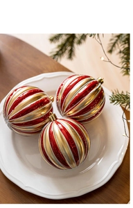 Détail de boules de Noël de 8cm rayées rouge et or sur une assiette blanche