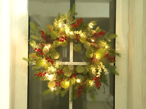 Close-up of a Christmas wreath with red berries and warm LED lights on a white window