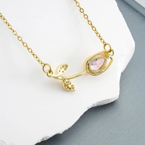 Elegant gold tulip necklace with pink stone and zircon on white decorative stone