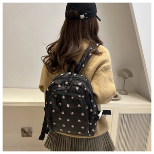 Model wearing a lightweight black floral backpack with pink blossoms in a lifestyle setting