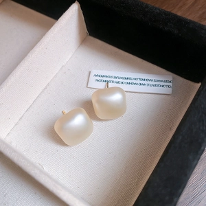 Detail view of matte square pearl earrings in cream finish on a jewelry box