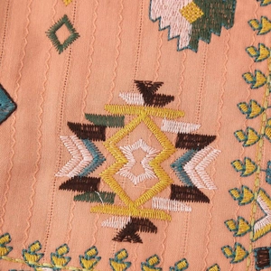 Ethnic embroidery on orange-pink vest featuring detailed geometric folk patterns