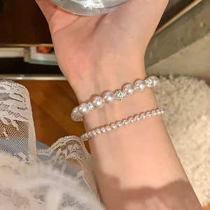 Détail de bracelets en perles blanches superposés avec perle sertie de diamants et micro perles