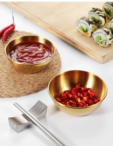 Close-up of golden stainless steel dipping sauce dishes on a dining table with sushi
