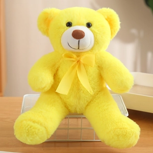 Cute bright yellow teddy bear plush toy with yellow ribbon bow sitting on a desk