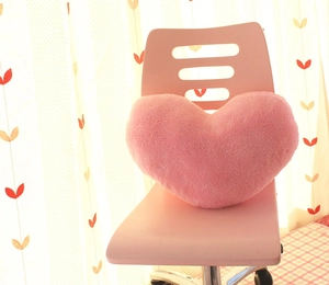 Close-up of a pink heart-shaped plush pillow placed on a matching pink chair