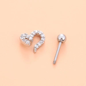 Macro shot of a silver heart-shaped ear stud with clear zircon insets on a soft peach background