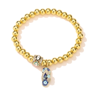 Gold-plated beaded bracelet with evil eye charm and flip-flop pendant on white backdrop