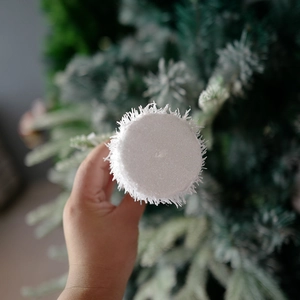 Handheld white snow Christmas ball ornament with plush texture on a green tree background