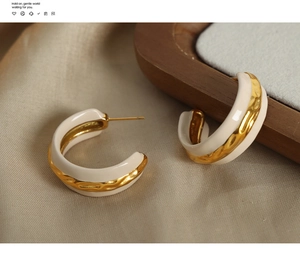 Macro shot of C-shaped cream enamel earrings with hammered gold texture on linen fabric