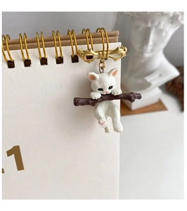 Macro detail of a cute white cat brooch hanging on a brown branch with a golden bow