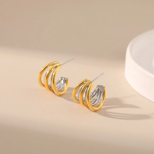 Detail of layered C-shaped earrings in two-tone gold and silver finish with studs