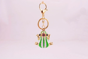 Detailed close-up of a green and white enamel frog keychain with golden metal finish