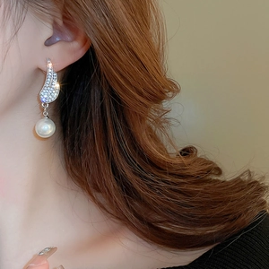 Close-up of diamond-encrusted angel wing earrings with dangling white pearls on model