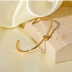 Dettaglio di un bracciale a nodo dorato su un supporto di pietra e seta elegante