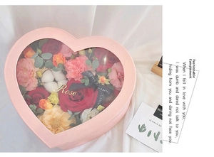 Macro shot of pink heart-shaped gift box with clear window and assorted faux roses