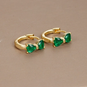 Macro shot of gold bow earrings with two teardrop emerald green zircons on a brown surface
