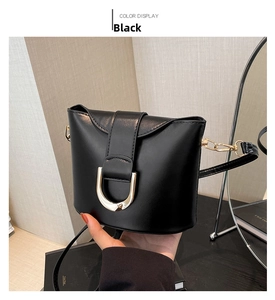 Close-up of black bucket bag with textured leather and large golden D-shaped metal buckle