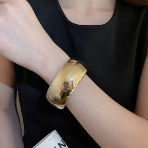 Gros plan d'un large bracelet manchette doré poli porté au poignet avec fini miroir