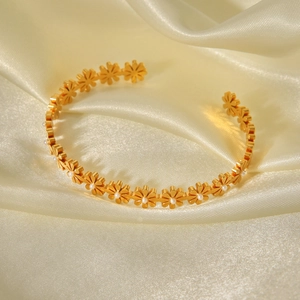 Detailed view of 18K gold daisy cuff bracelet with pearls on champagne satin fabric