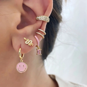 Close-up of pink enamel smile earrings and gold zircon snake studs set on ear