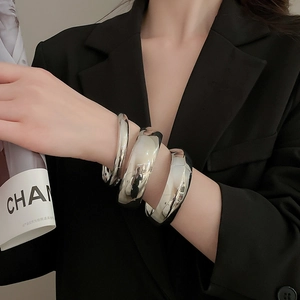 Gros plan de trois bracelets joncs en métal argenté poli portés sur une manche de blazer
